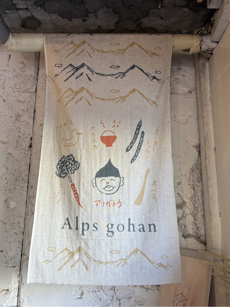 店名「Alps gohan」と柔らかいイラストが描かれたタペストリー